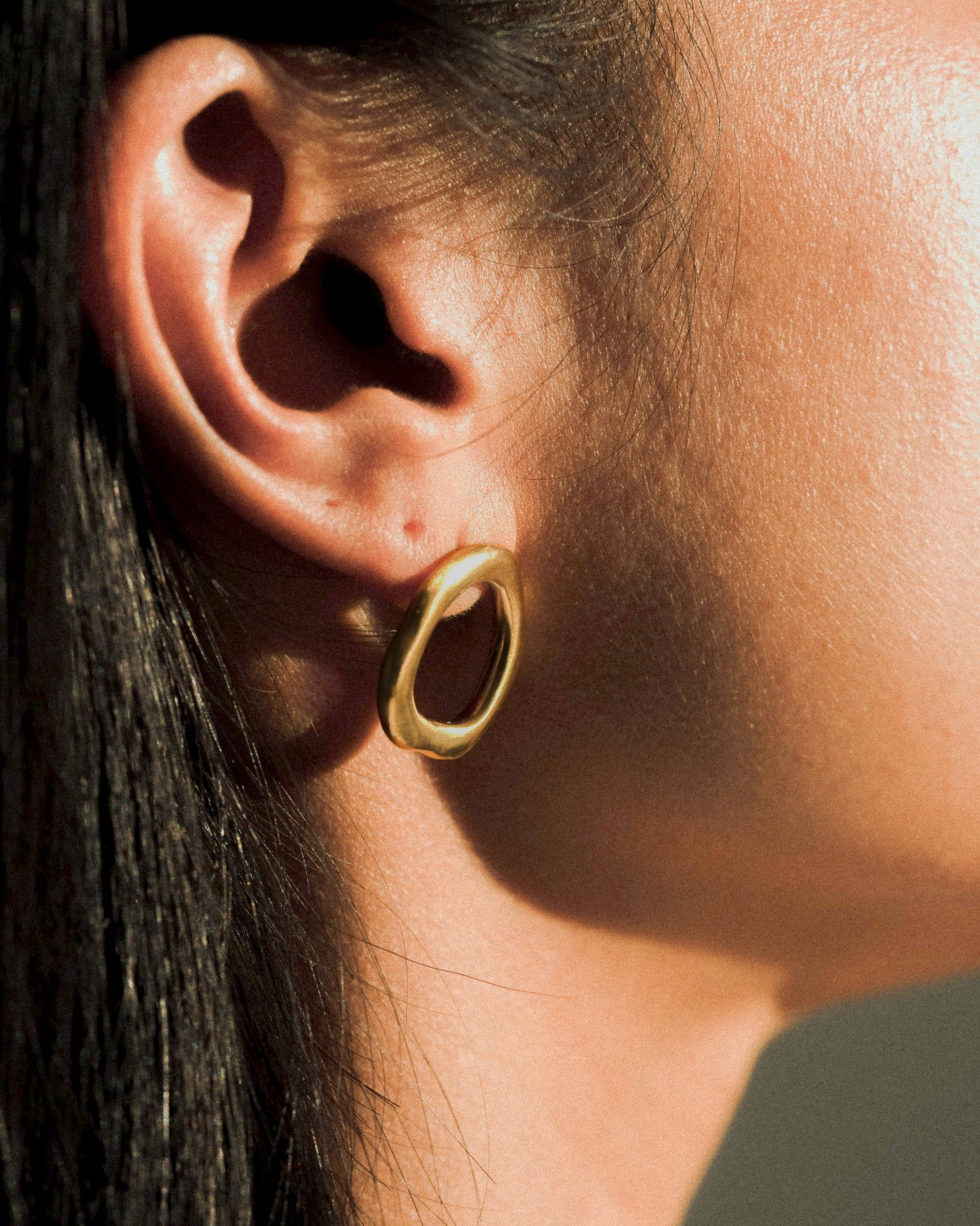 A model wearing a pair of organic and sculptural oval brass earrings.