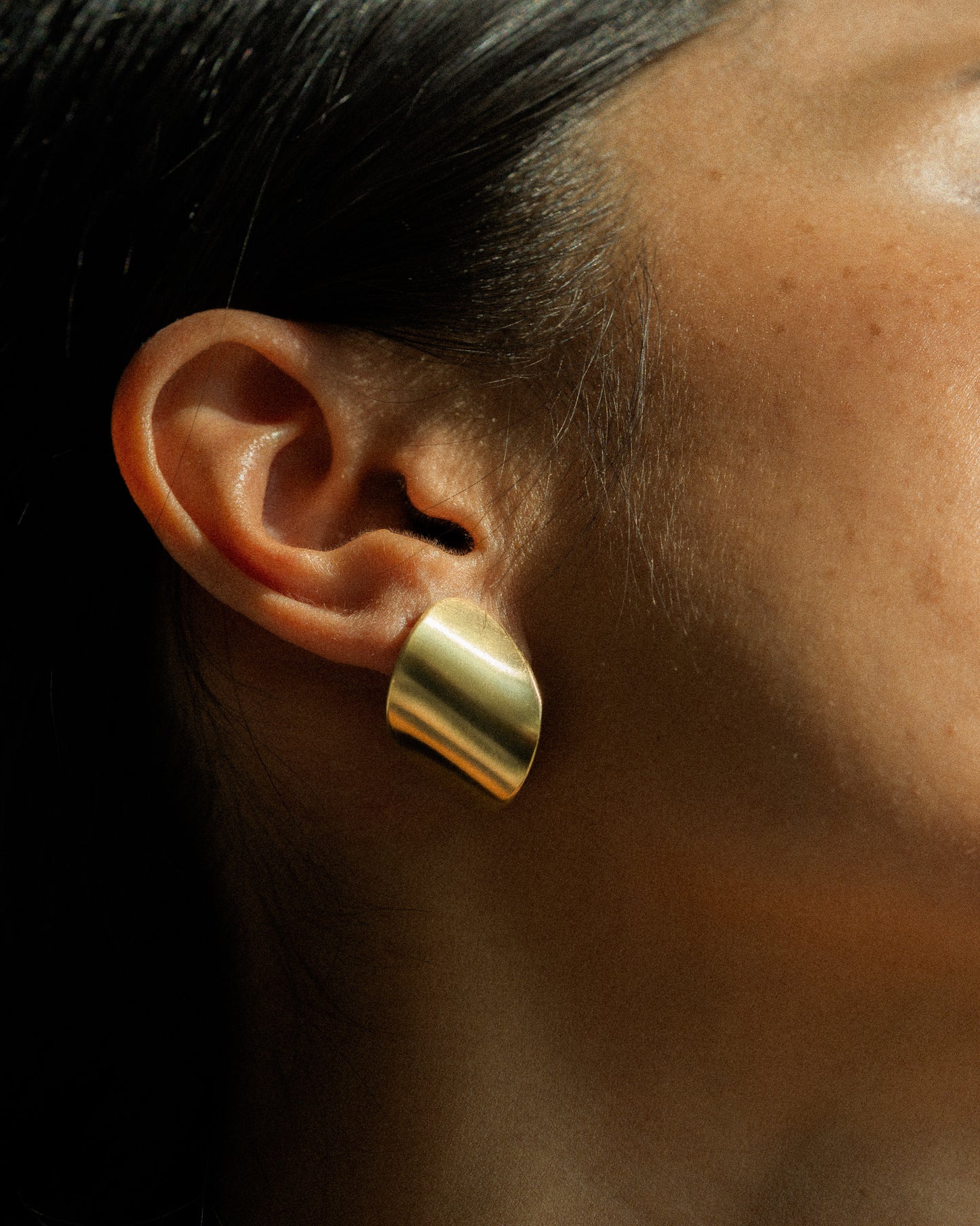 A model a pair of clean line and leaf-shaped brass earrings.