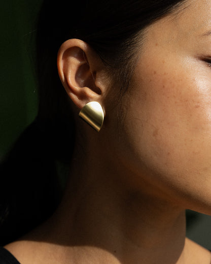 A model wearing a pair of clean line and leaf-shaped brass earrings.