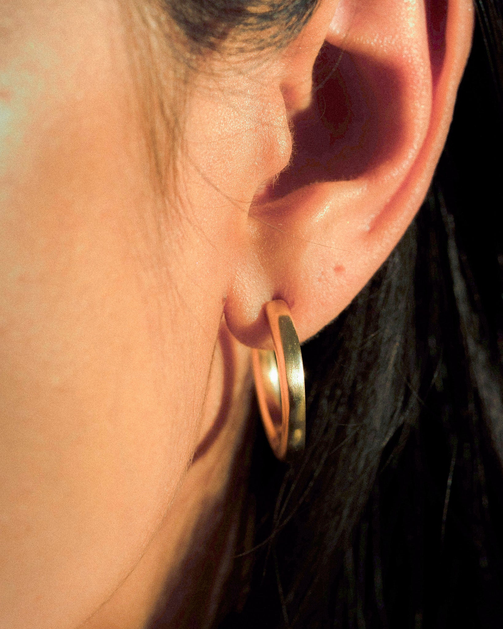 A model wearing a pair of organic textured and fluid brass hoops.