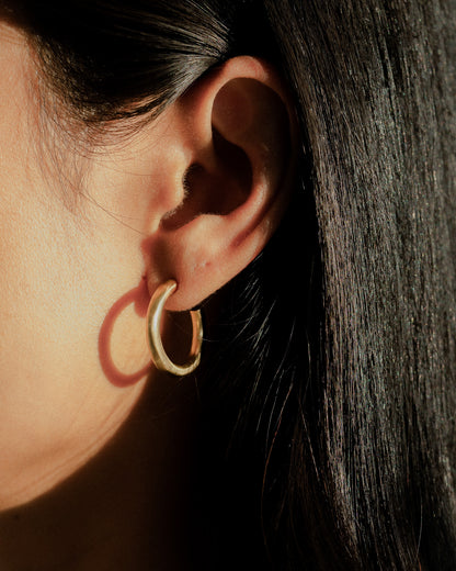 A model wearing a pair of organic textured and fluid brass hoops.