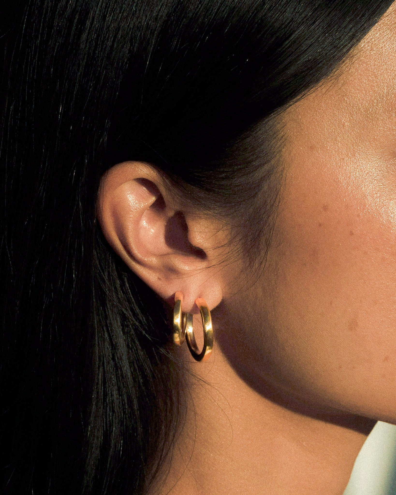 A model wearing a small and large pair of organic textured and fluid brass hoops.