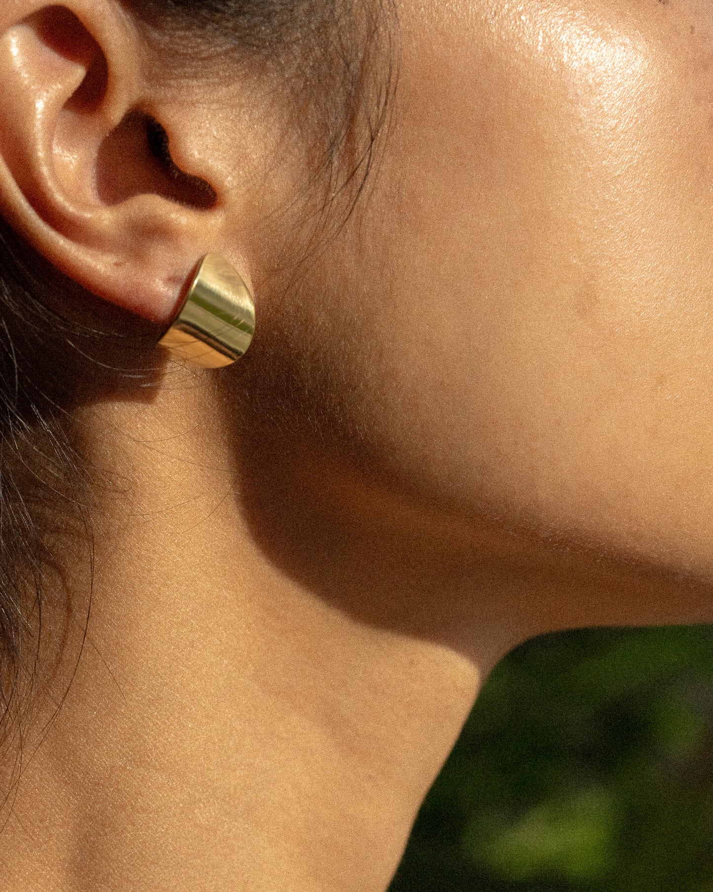 A model wearing a small pair of clean line and leaf-shaped brass earrings.