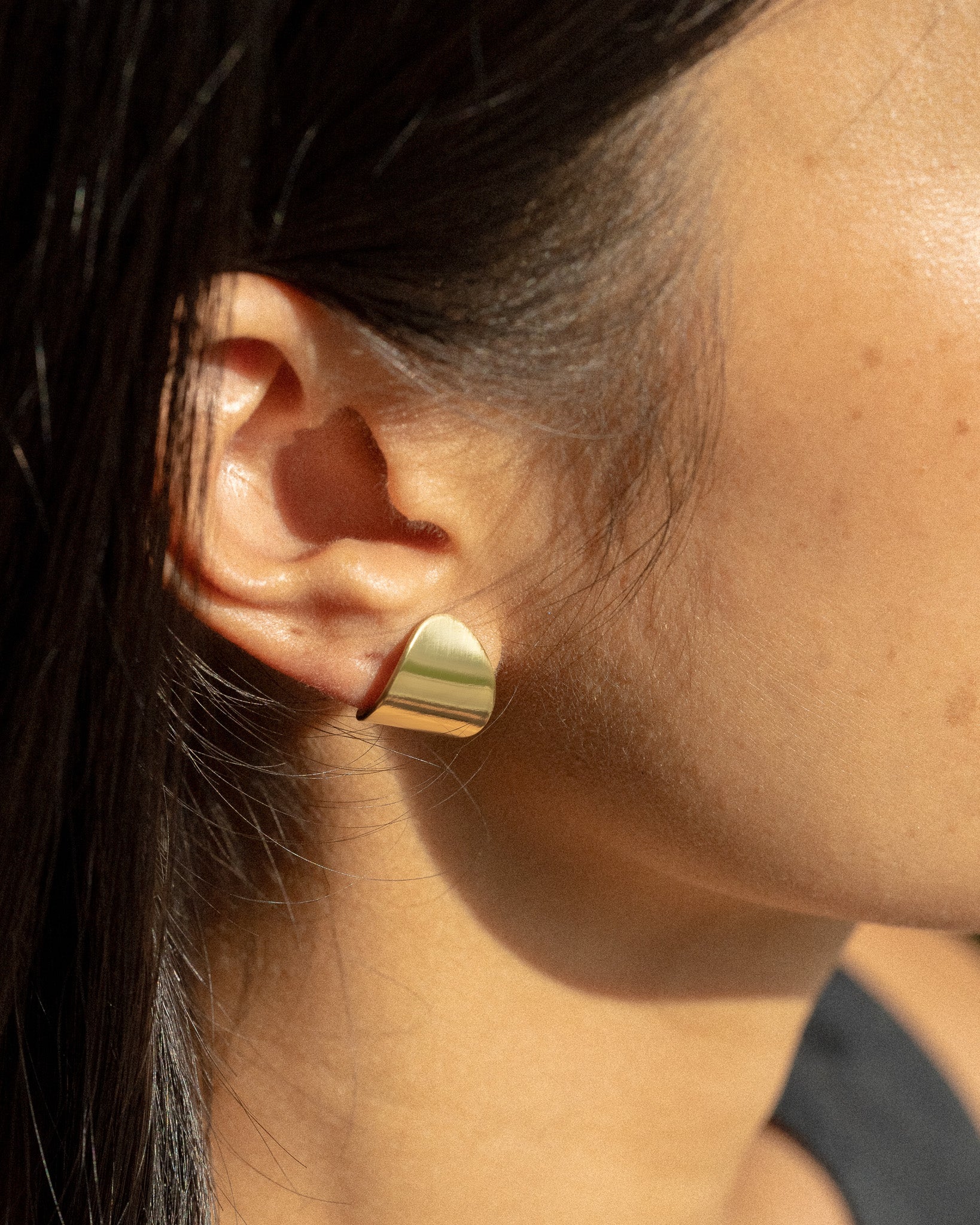 A model wearing a small pair of clean line and leaf-shaped brass earrings.