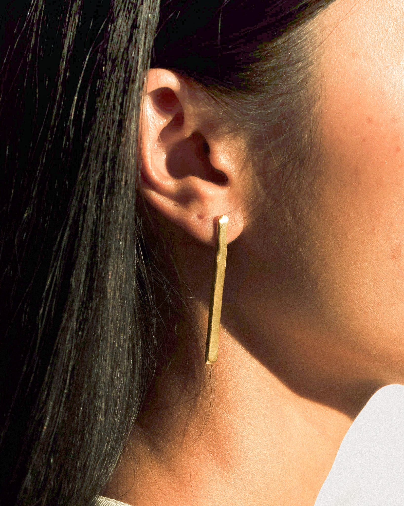 A model wearing a pair of straight line  and soft curved brass earrings.