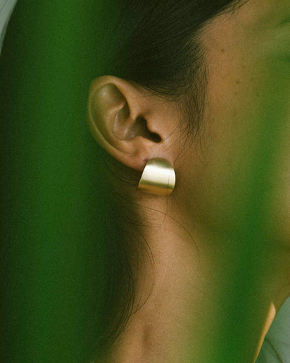 A model wearing a pair of curved and oval pebble-shaped earrings.