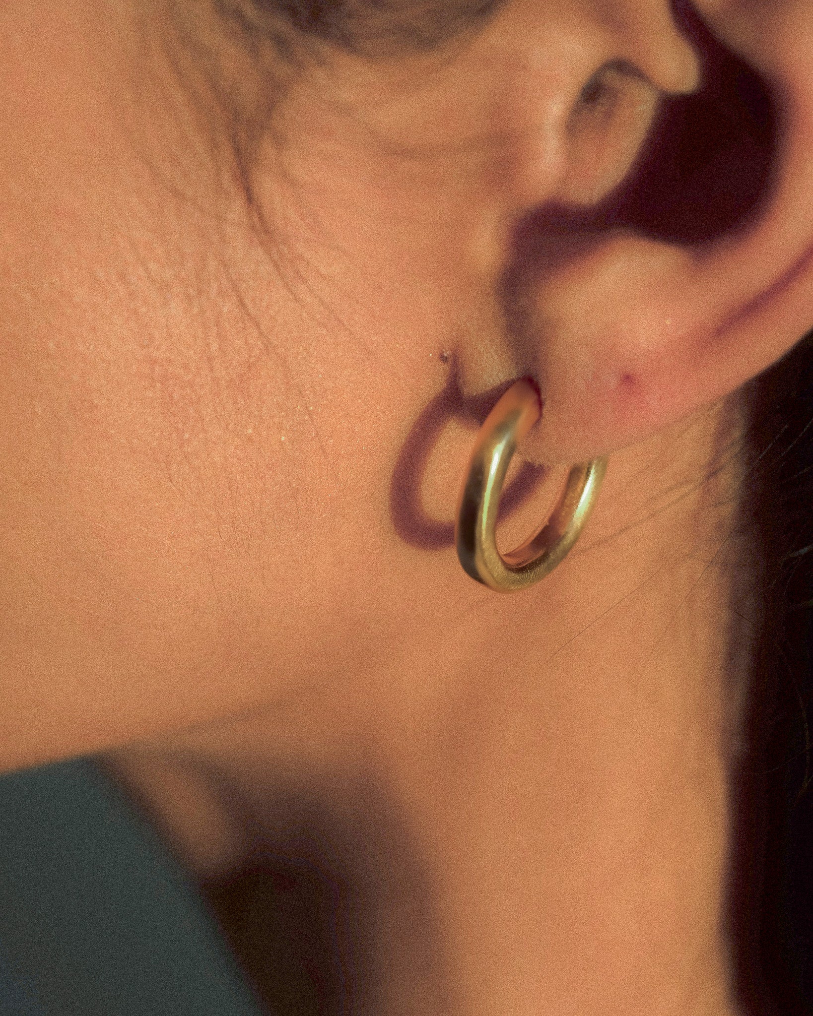 A model wearing a pair of organic textured and fluid  formed brass hoops.